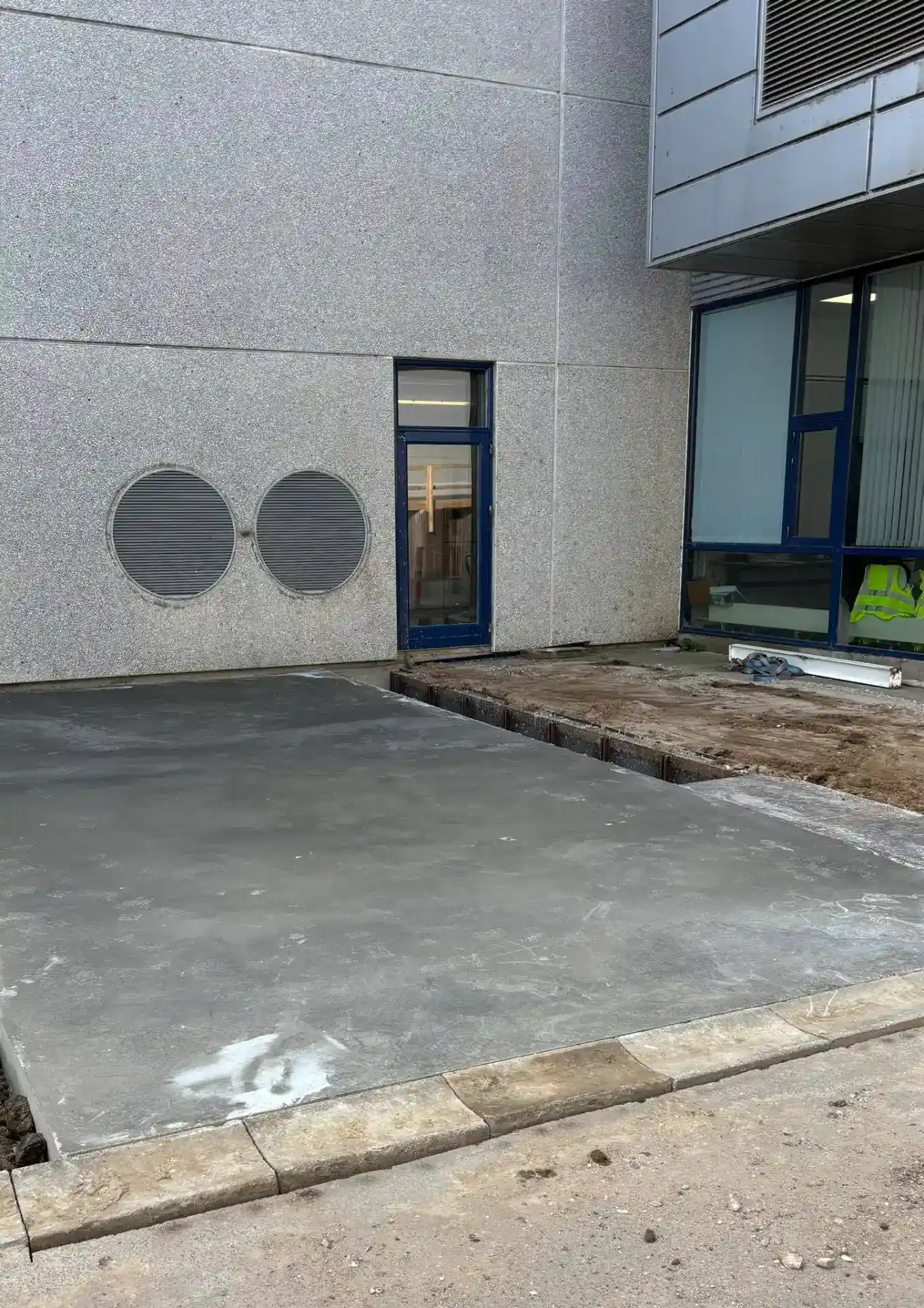 Ny betonbelægning foran erhvervsbygning med moderne facade.