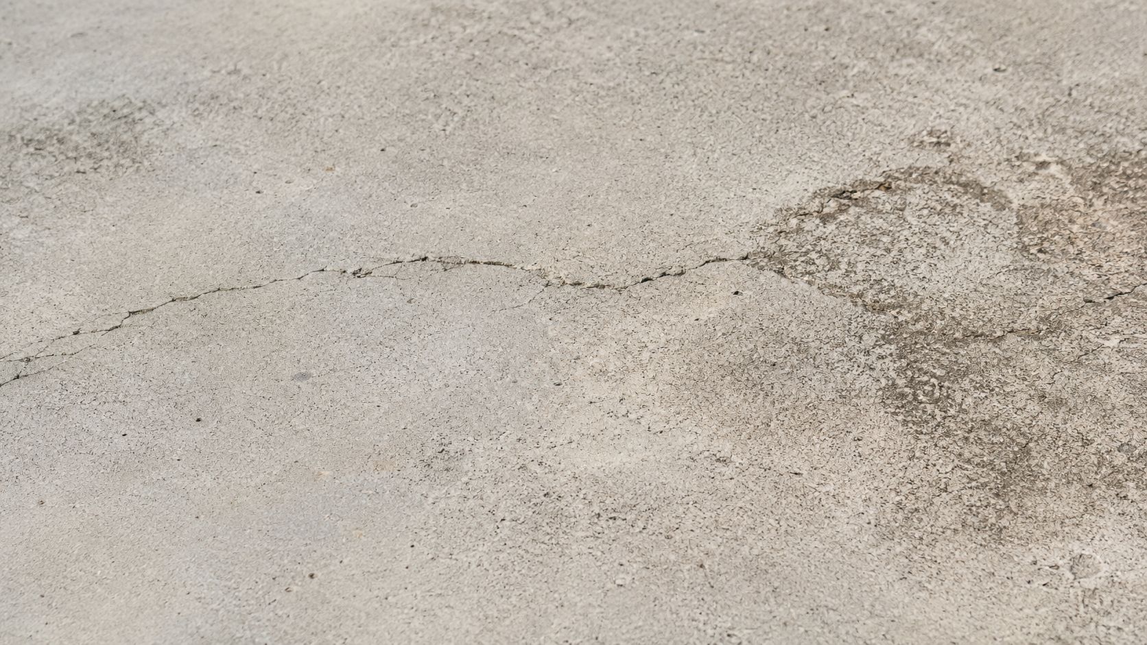En grå overflade af beton med en synlig revne, der løber hen over det ujævne udendørs terræn.