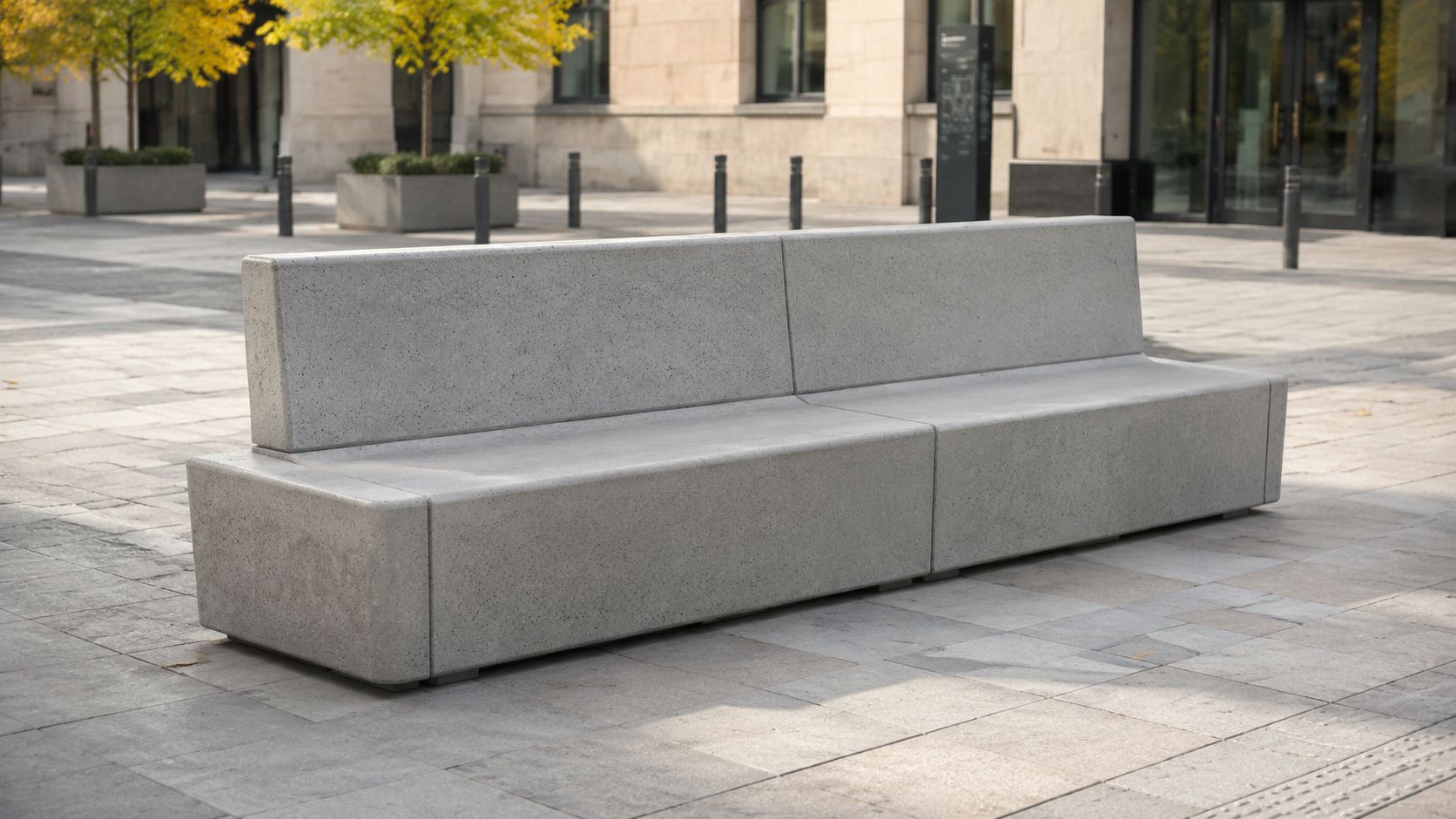 En moderne og minimalistisk udendørs bænk lavet af grå beton placeret på en flisebelagt plads foran bygningen.
