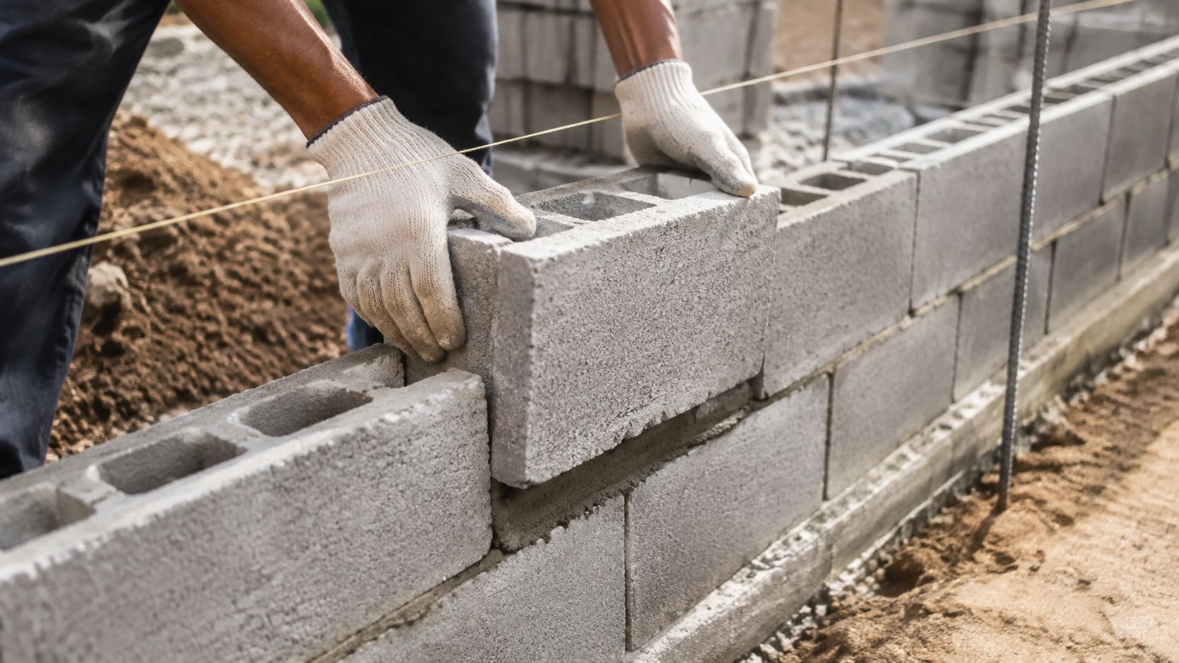 En bygningsarbejder bygger en støttemur af betonblokke på en byggeplads ved hjælp af en rettesnor.